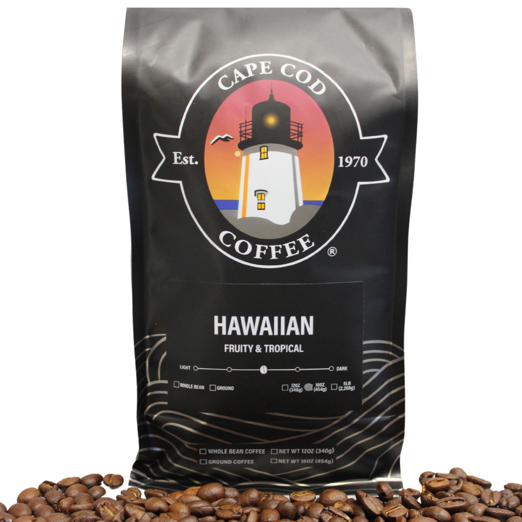 A bag of Cape Cod Coffee Hawaiian, featuring a black color scheme with white and orange graphics, including a lighthouse, and text indicating the coffee is fruity and tropical.