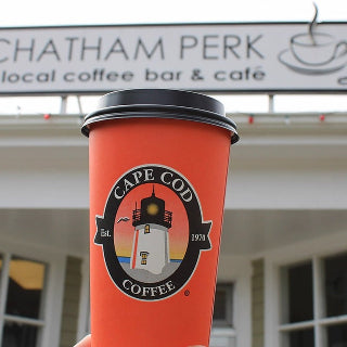 Orange Cape Cod Coffee cup held in front of a Chatham Perk coffee shop.