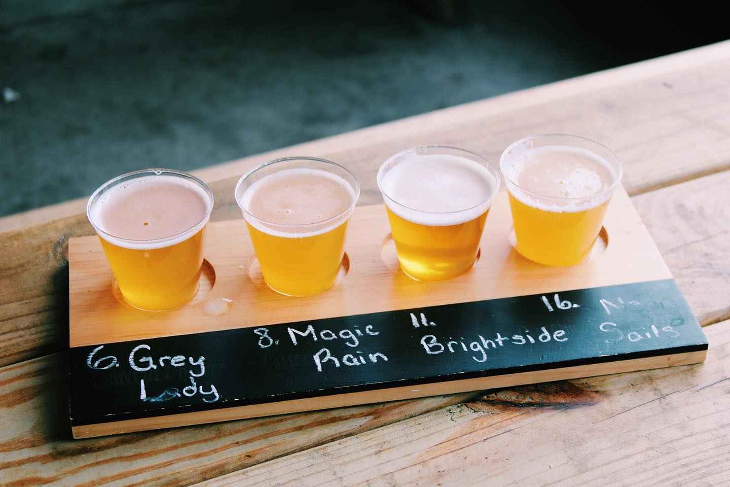 An image of a wooden plank with small shots of beer on them, called a beer flight. There are 4 beer samples.