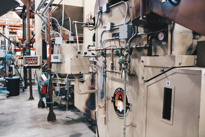 Photo of machinery with the Cape Cod Coffee lighthouse logo. The machinery is coffee bean roasting equipment. 
