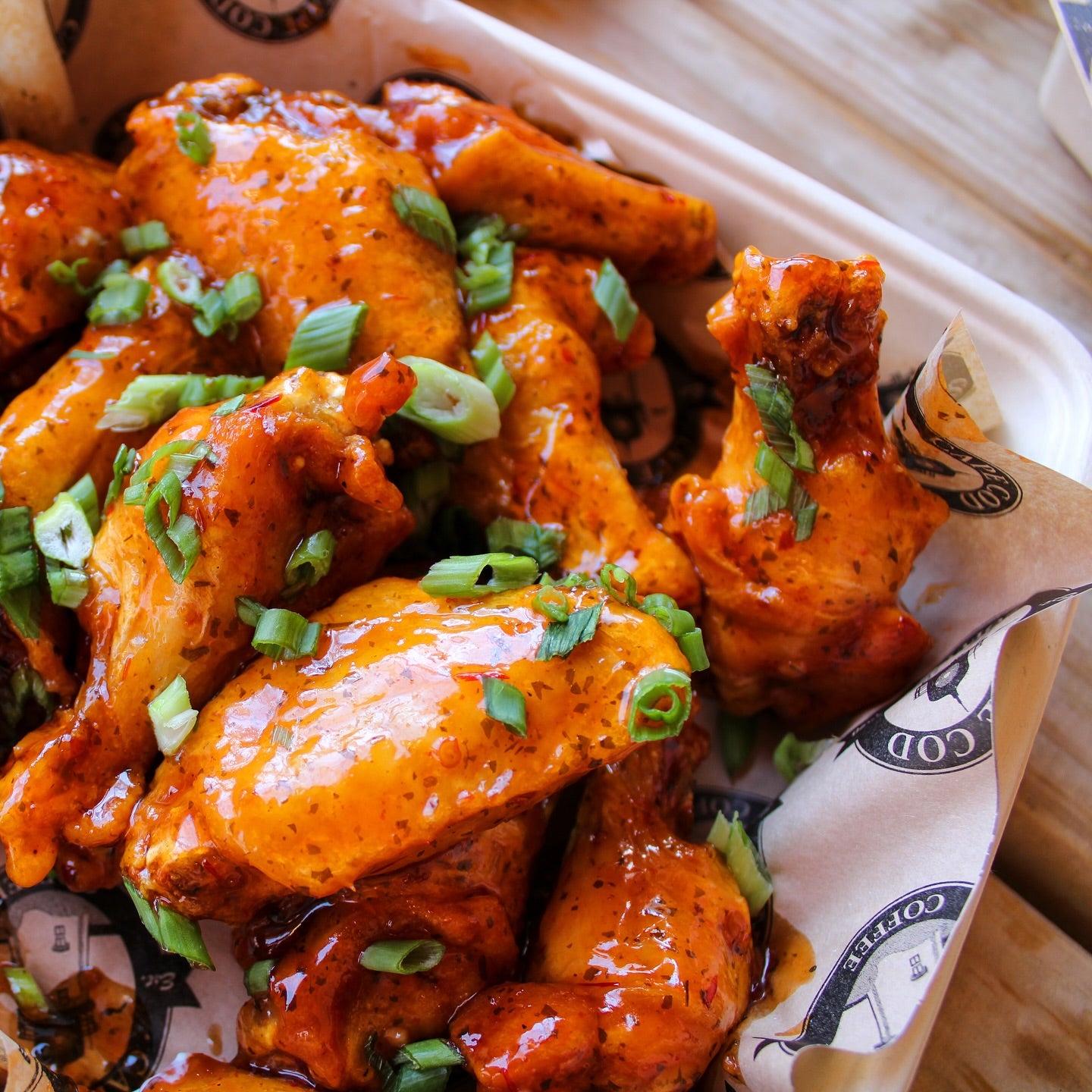 An image of chicken wings with scallions in a basket with the logo "Cape Cod Coffee" on it.