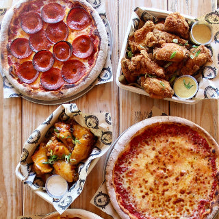 Two pizzas and two baskets of fried chicken on a wooden table served at the Route 130 Mashpee Cape Cod Coffee Location